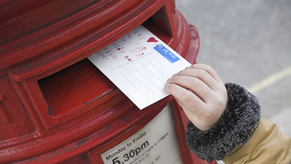Tiny hand pushing a postcard inside a postbox
